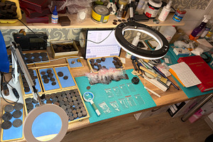 A cluttered workspace with coins, magnifying glass, and tools for coin examinat, an Industrial Photo by Textures & Backgrounds