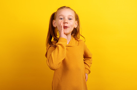 Young girl in mustard sweater with hand by mouth, appearing to w