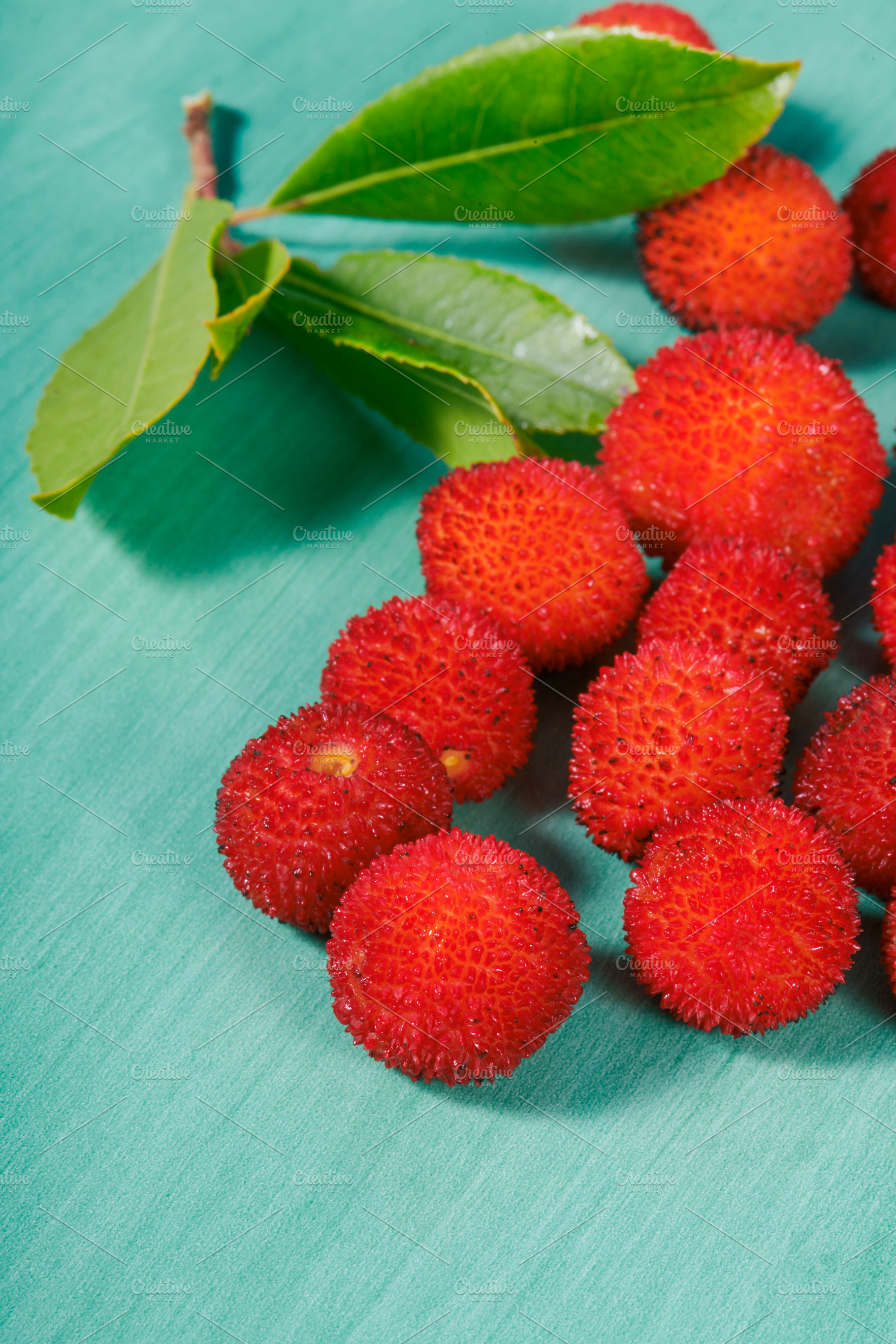 arbutus berries with leaves on a turquoise surface, a Photo by Nito
