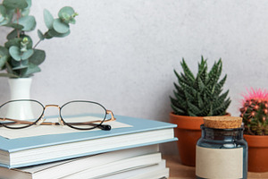 Eyeglasses resting on stack of books with plants and pen on wood, a Business Photo by Olena Rudo