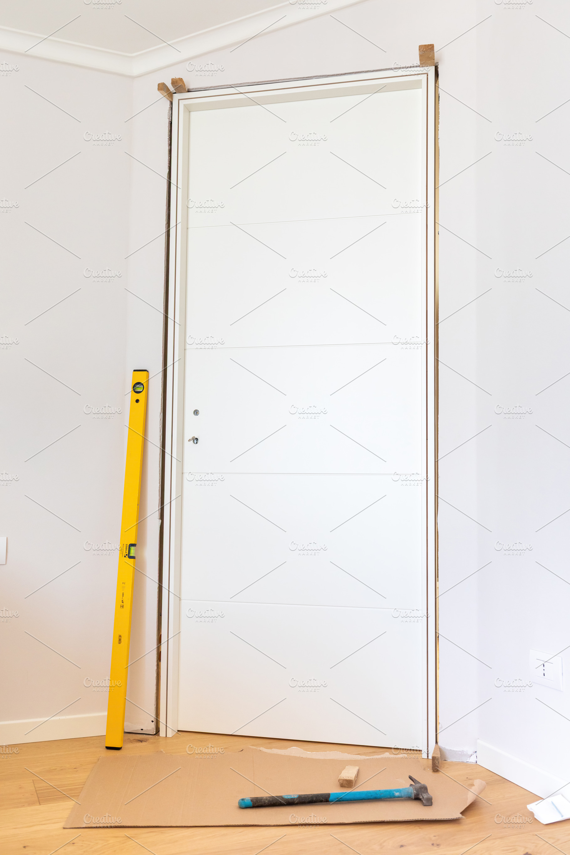 Carpenter Installing Modern White Door with Level and Hammer, an Architecture Photo by Antonio Gravante Market