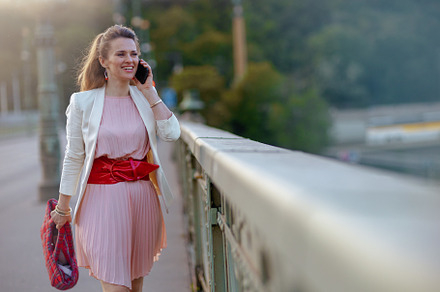 smiling woman in dress and jacket in city using phone, a Person Photo by Alliance Images