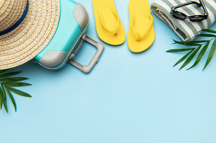 Suitcase, beach towel, flip flops, sunglasses and a straw hat su