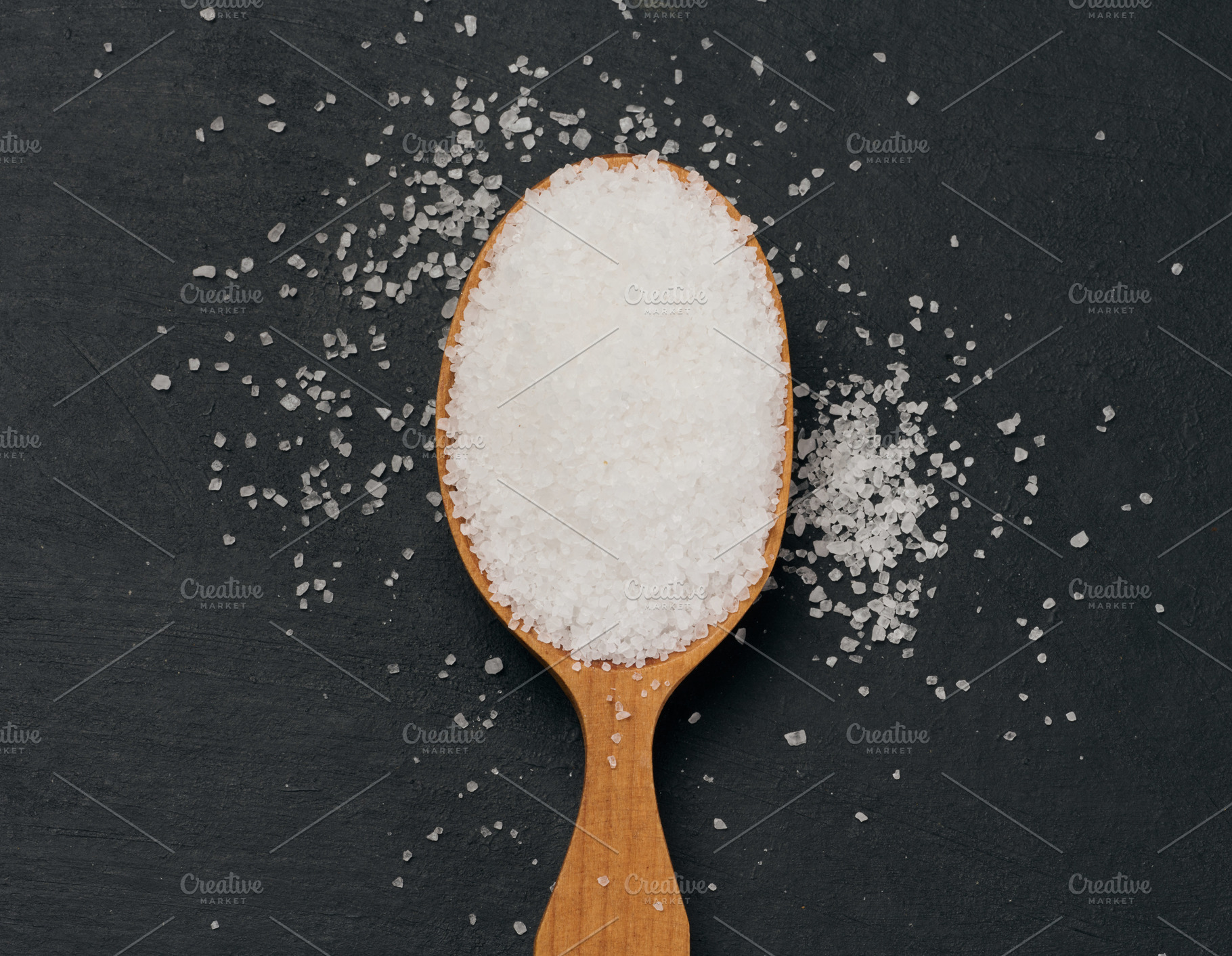 Handful of salt in a wooden spoon on a black table, top view, a Food & Drink Photo by ndanko