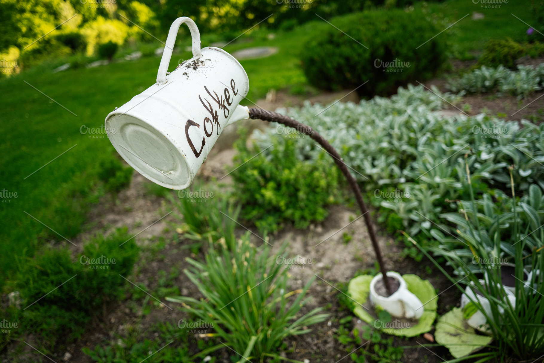 Decorative outdoor installation of a coffee mug in a lush green garden, a Photo by AS photostudio
