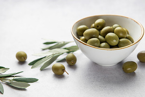 Fresh green olives in a bowl with olive branches on marble table, a Food & Drink Photo by Olena Rudo