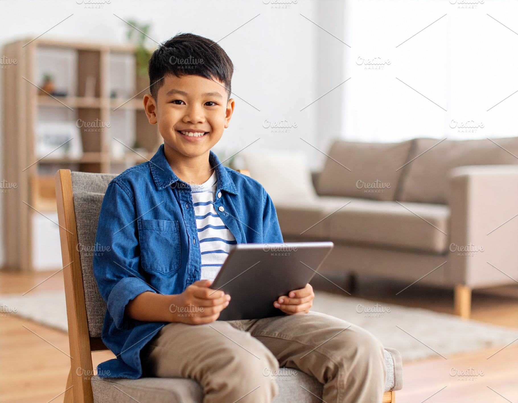 Boy with a tablet sitting on chair at living room while smiling, a Person Photo by DanFLCreativo