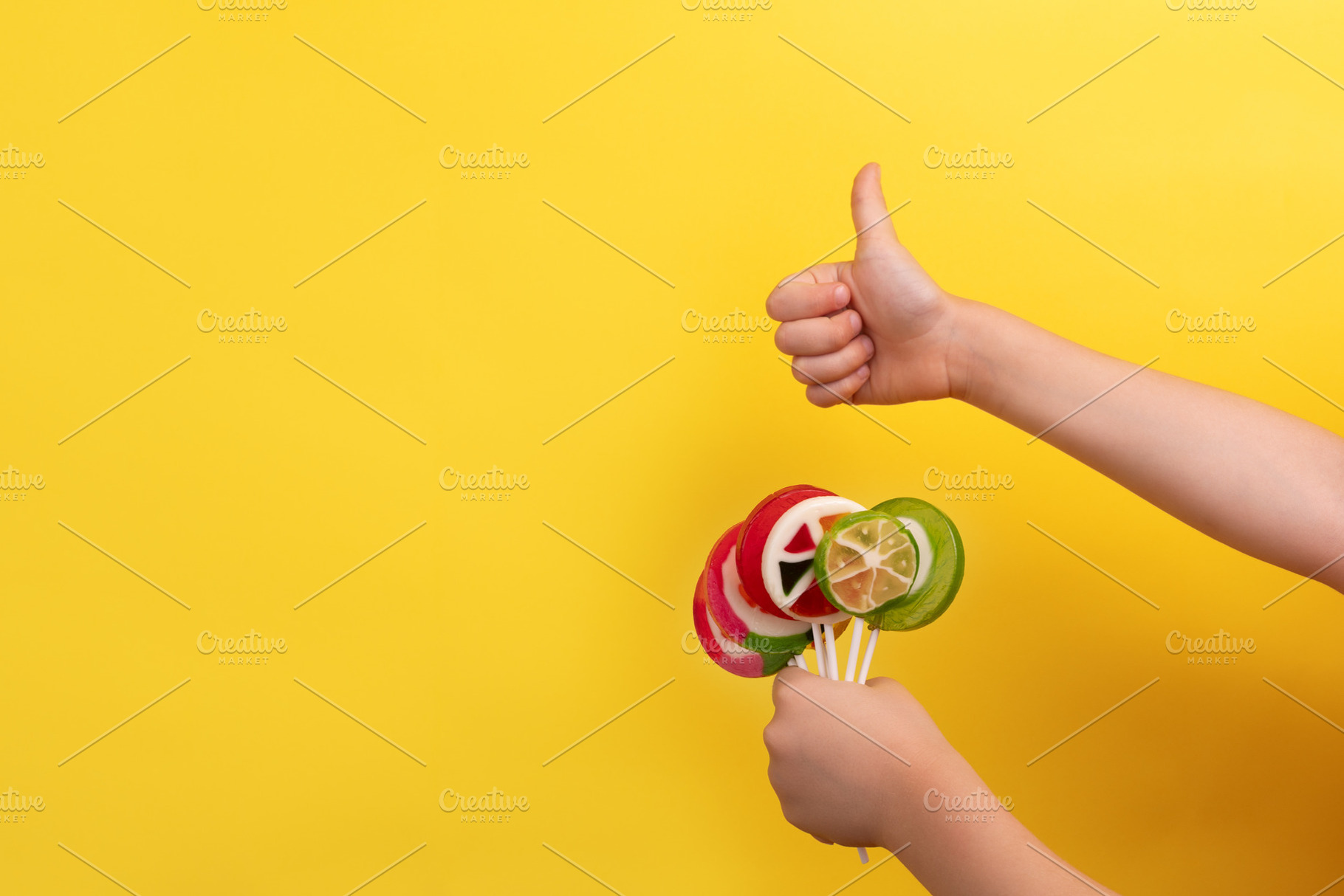 Child's hands holding colorful lollipops and giving a thumbs up, a Food & Drink Photo by Ales Munt
