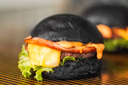Black Beef burger filled with cheese and vegetables placed on a wooden table, a Food & Drink Photo by Half Production