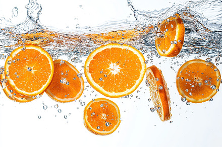 Sliced orange falling into water on white background, a Food & Drink Photo by AlyaAnd