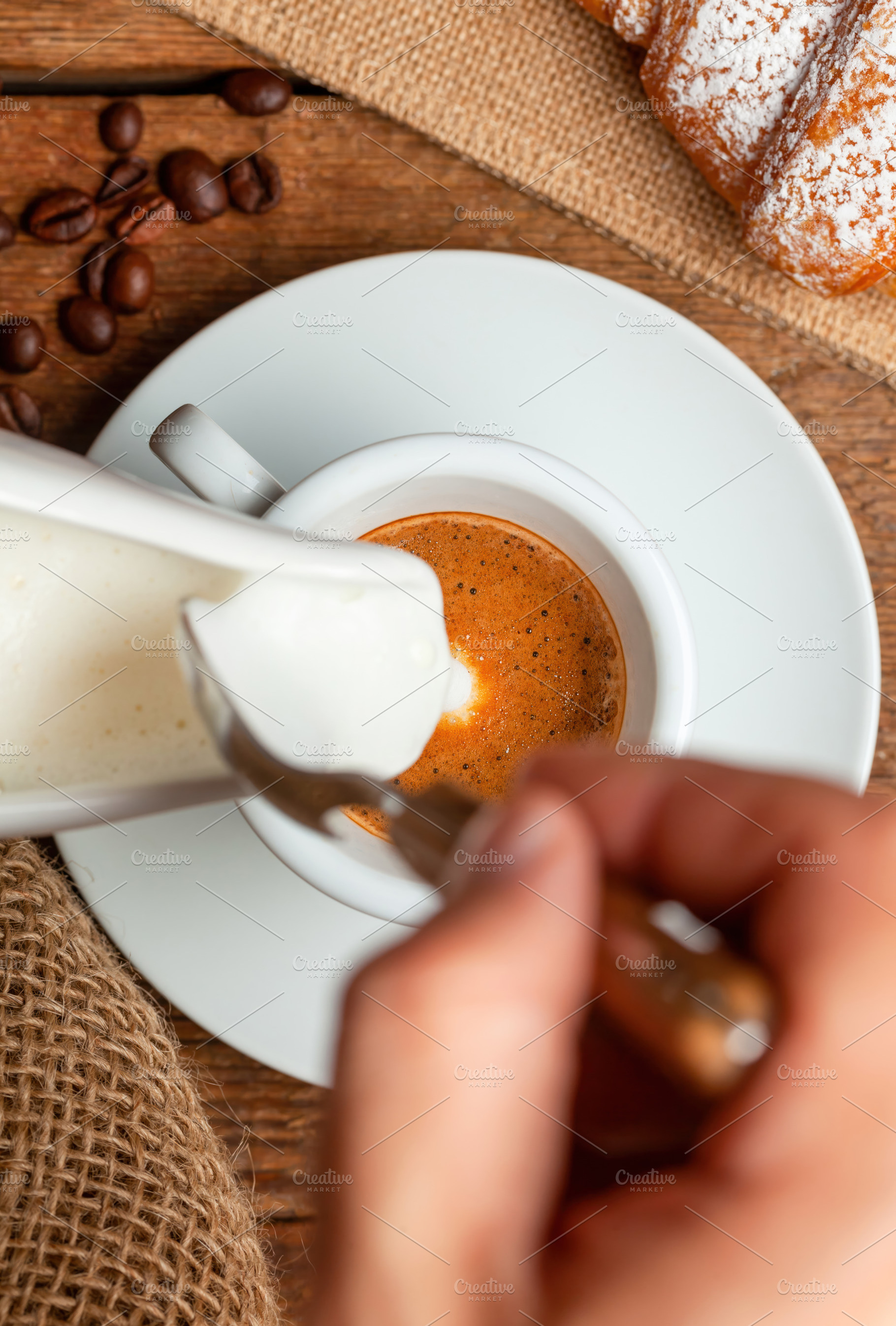 Barista pouring milk into espresso macchiato with croissant and coffee beans on, a Food & Drink Photo by Antonio Gravante Market