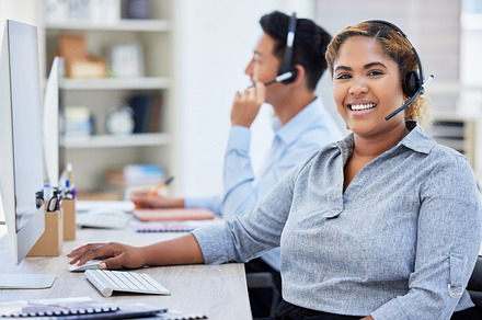 Young happy mixed race female call center agent working on a computer while answering calls in an office at work. Hispanic female customer service agent smiling wearing a headset on a call, a Photo by Peopleimages.com