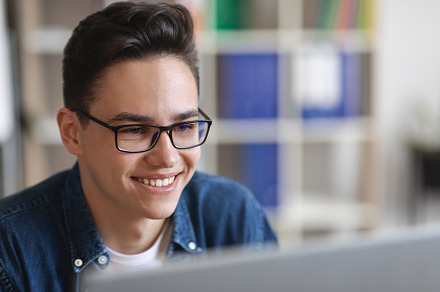 Closeup Of Smiling Young Man In Glasses Working With Laptop In Office, a Photo by Prostock-Studio