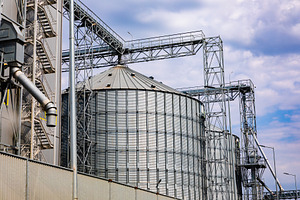 Large metallic grain silos and industrial structures under a cloudy sky, ideal, an Industrial Photo by Ales Munt
