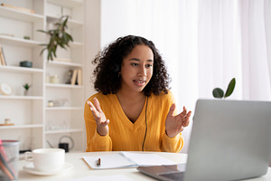 Cheerful young black woman in headphones making video call on laptop at home, a Photo by Prostock-Studio