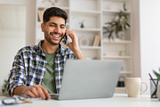 Smiling Arab man working and talking on phone at home, a Photo by Prostock-Studio (Thumbnail 1 of 2)