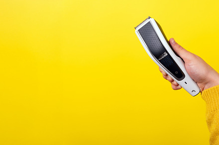 Hand holding an electric hair trimmer against vibrant yellow bac