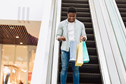 Happy black man holding shopping bags looking inside, a Photo by Prostock-Studio (Thumbnail 3 of 3)
