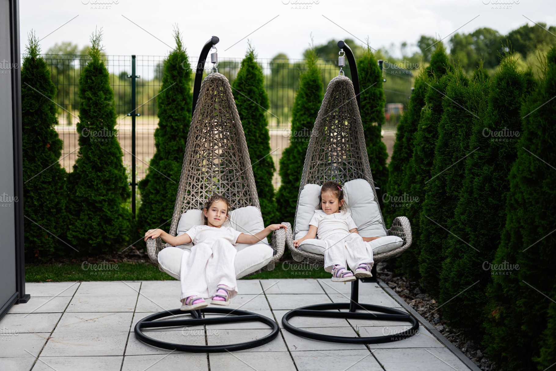 Two children relax on patio egg chairs surrounded by lush green garden., a Photo by AS photostudio