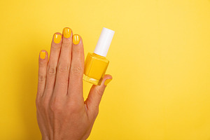 Female hand with glossy yellow nail polish holding matching bott, a Beauty & Fashion Photo by Ales Munt