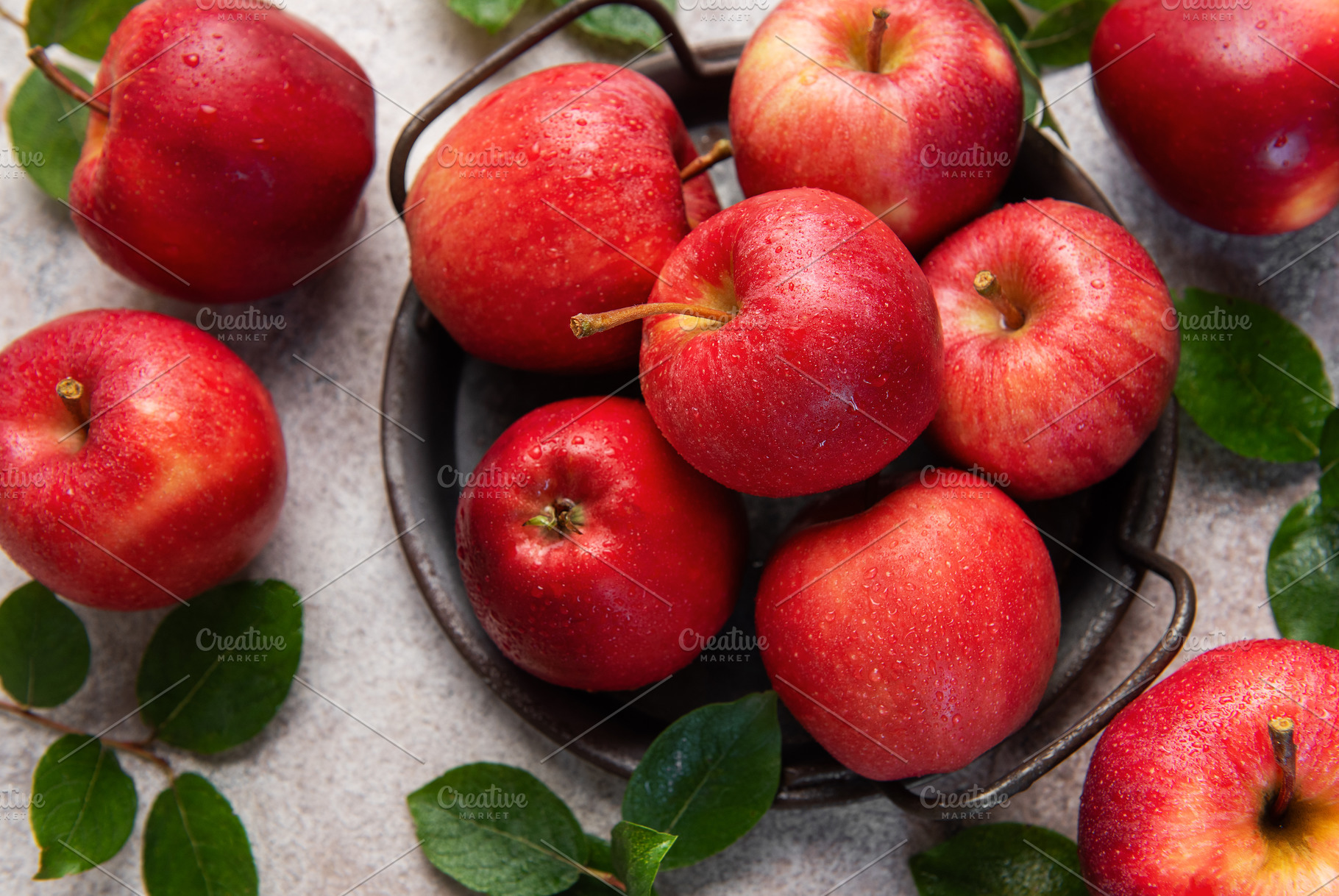 Fresh red apples with green leaves resting in a metal basket, a Food & Drink Photo by Olena Rudo