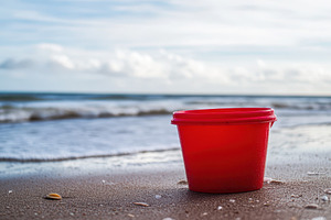 Vibrant red bucket on sandy beach, a Photo by Pavel_design