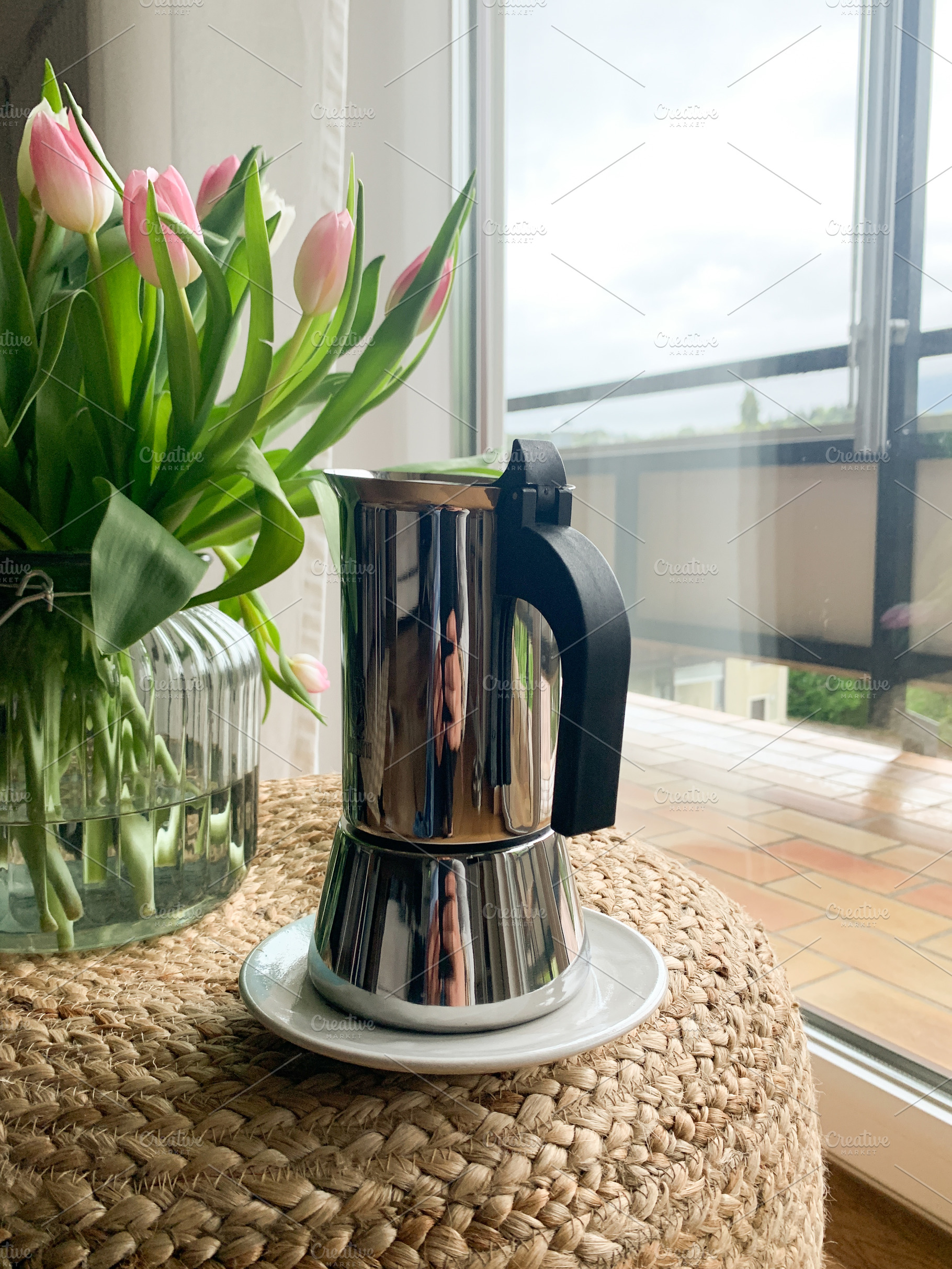 A moka pot and tulips on a woven stool near a bright window., a Background Photo by sebastianaraw