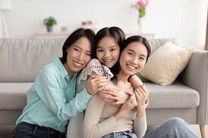 Young Asian woman with her cute daughter and mature mother hugging and smiling, a Photo by Prostock-Studio