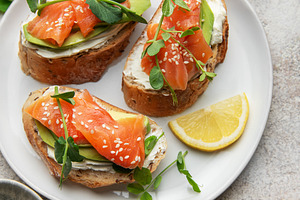 Salmon avocado toasts with cream cheese and lemon on plate, a Food & Drink Photo by Olena Rudo