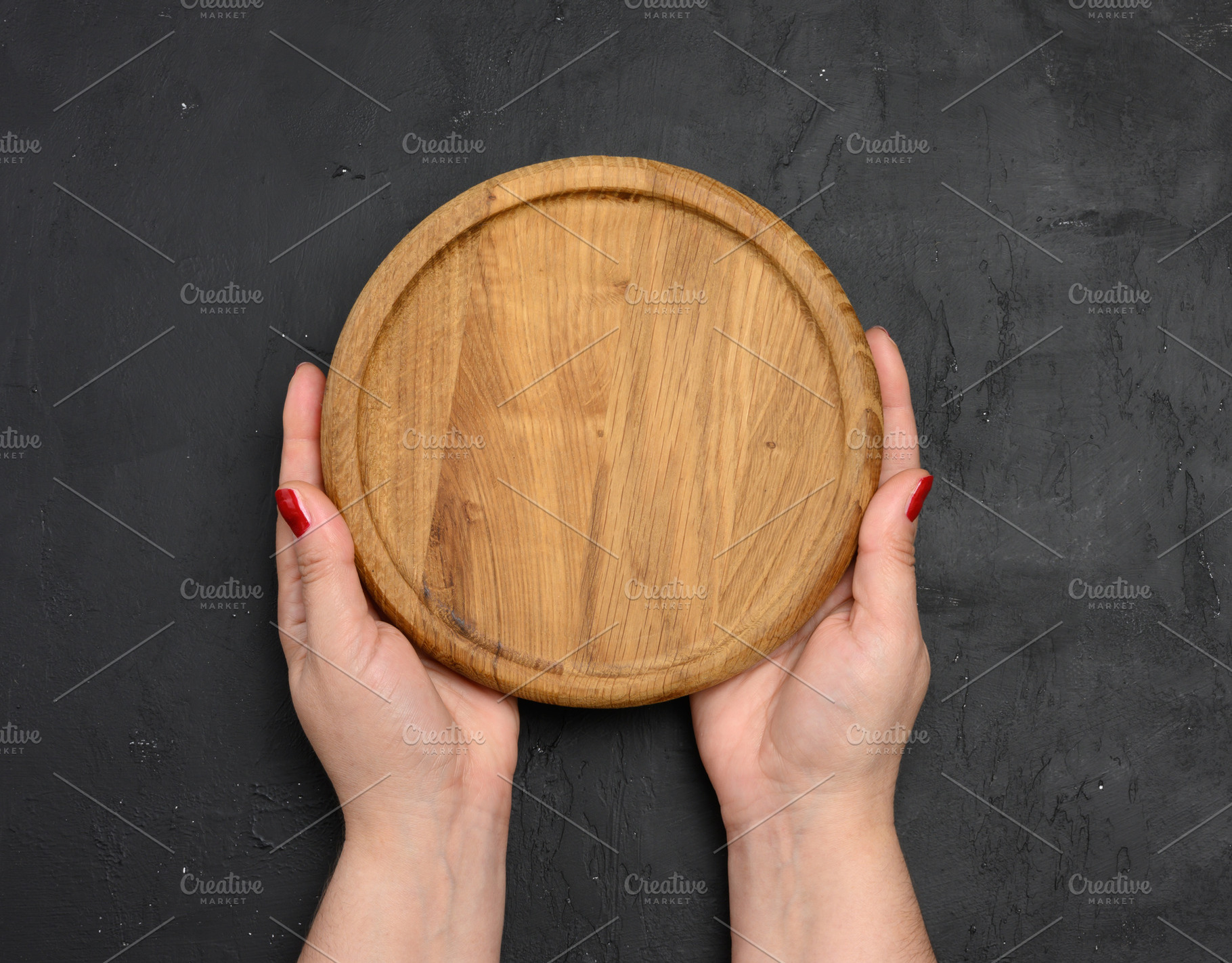Female hand holding round wooden blank board on black background, a Food & Drink Photo by ndanko
