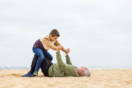 Funny boy and his grandfather playing stretched out in the sand, a Photo by Cosca