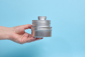 A person holding a pyramid of three round aluminum jars on their