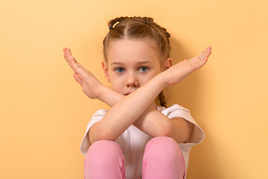 Young girl with braided hair crossing arms in an X sign, seated, a Person Photo by Ales Munt