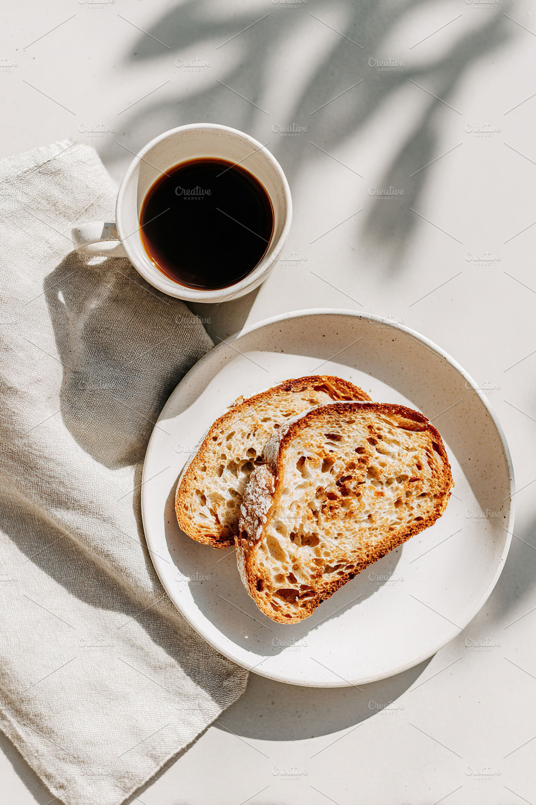 Enjoying coffee with toasted bread on a white ceramic plate in morning light, a Photo by AlyaAnd