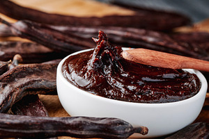 a wooden spoon stirs thick carob spread in a bowl, a Photo by Nito