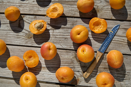 Halved and whole apricots with knife on rustic wooden table