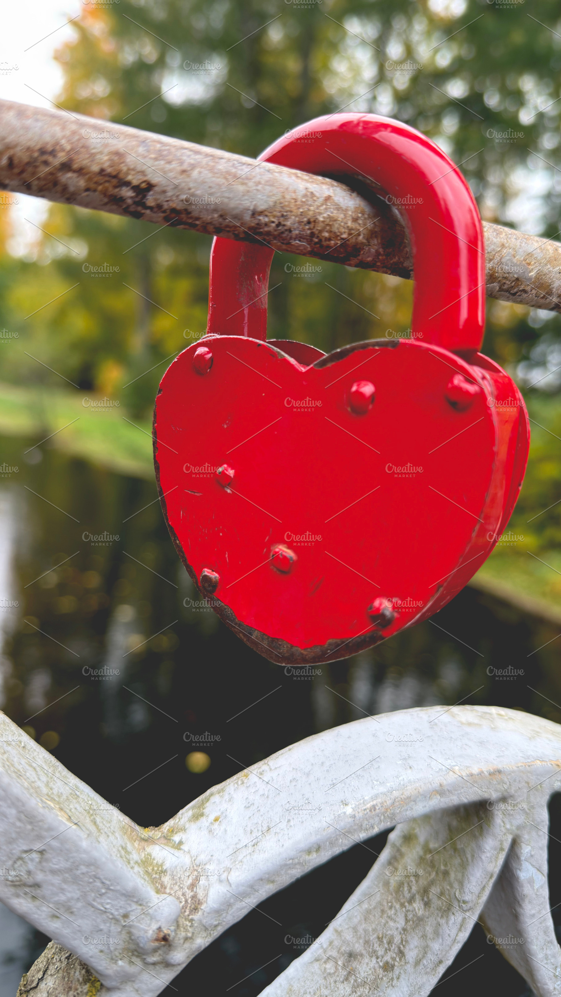 A red heart-shaped padlock attached to a metal railing with a blurred natural b, an Industrial Photo by Textures & Backgrounds