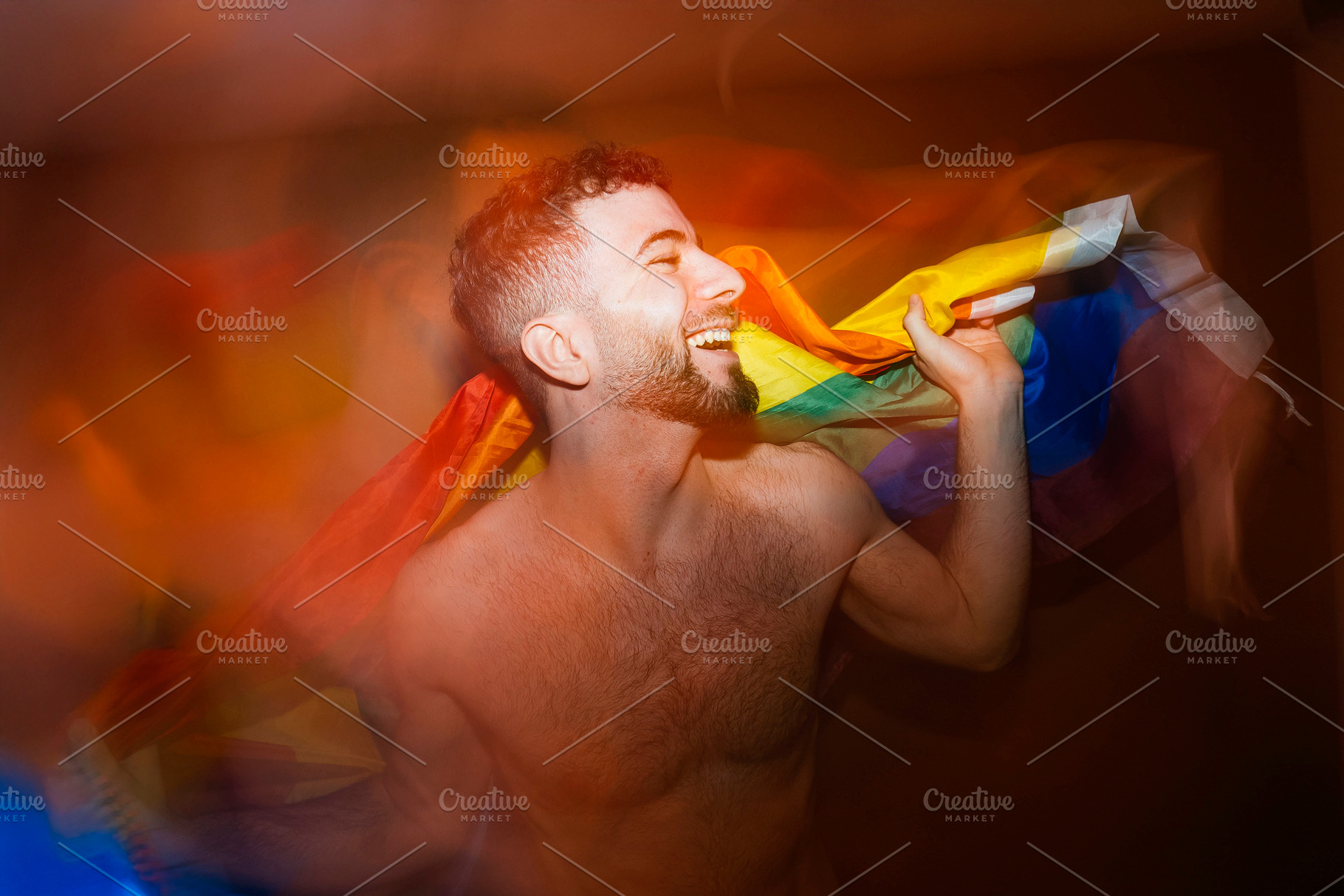 Young adult man smiling celebrating lgbtq+ pride with rainbow flag, a Photo by karrastock