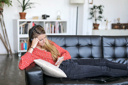 Blonde woman using mobile and listening music by headphones while lying on leat, a Person Photo by 2Design
