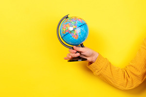Person holding a colorful globe against a vibrant yellow backgro, a School & Education Photo by Ales Munt
