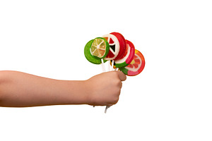 Child’s hand holding colorful fruit lollipops, isolated on whi, a Food & Drink Photo by Ales Munt