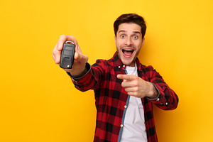 Excited Man Holding Car Key And Pointing, Yellow Background