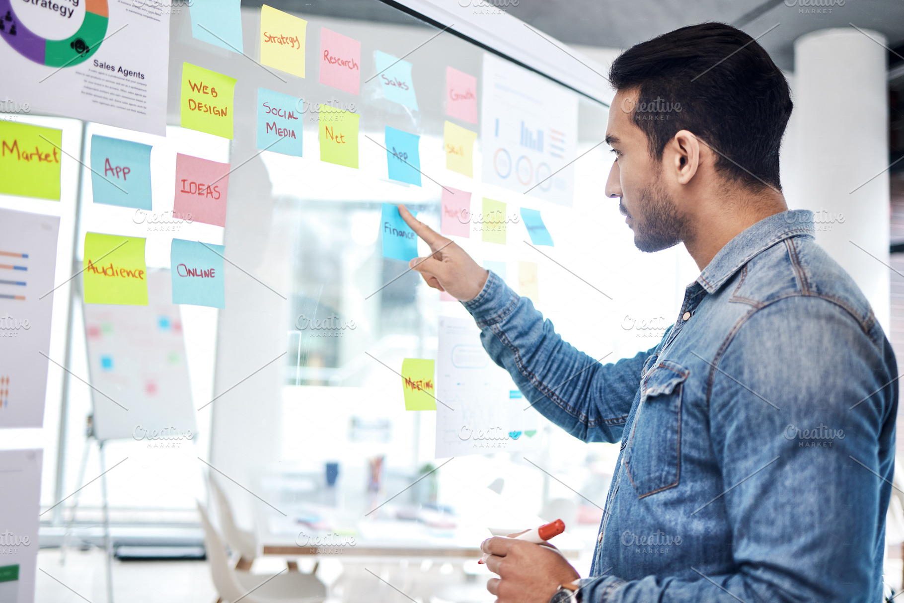 Creative man, sticky note and pointing on glass board for schedule tasks, planning or brainstorming at office. Male person or employee with plan, agenda or marketing strategy for startup at workplace, a Photo by Peopleimages.com
