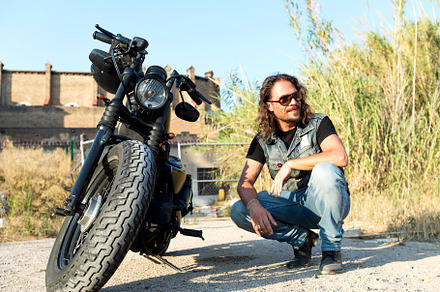Young male wearing sunglasses crouched next to a chopper motorcycle, a Person Photo by 2Design