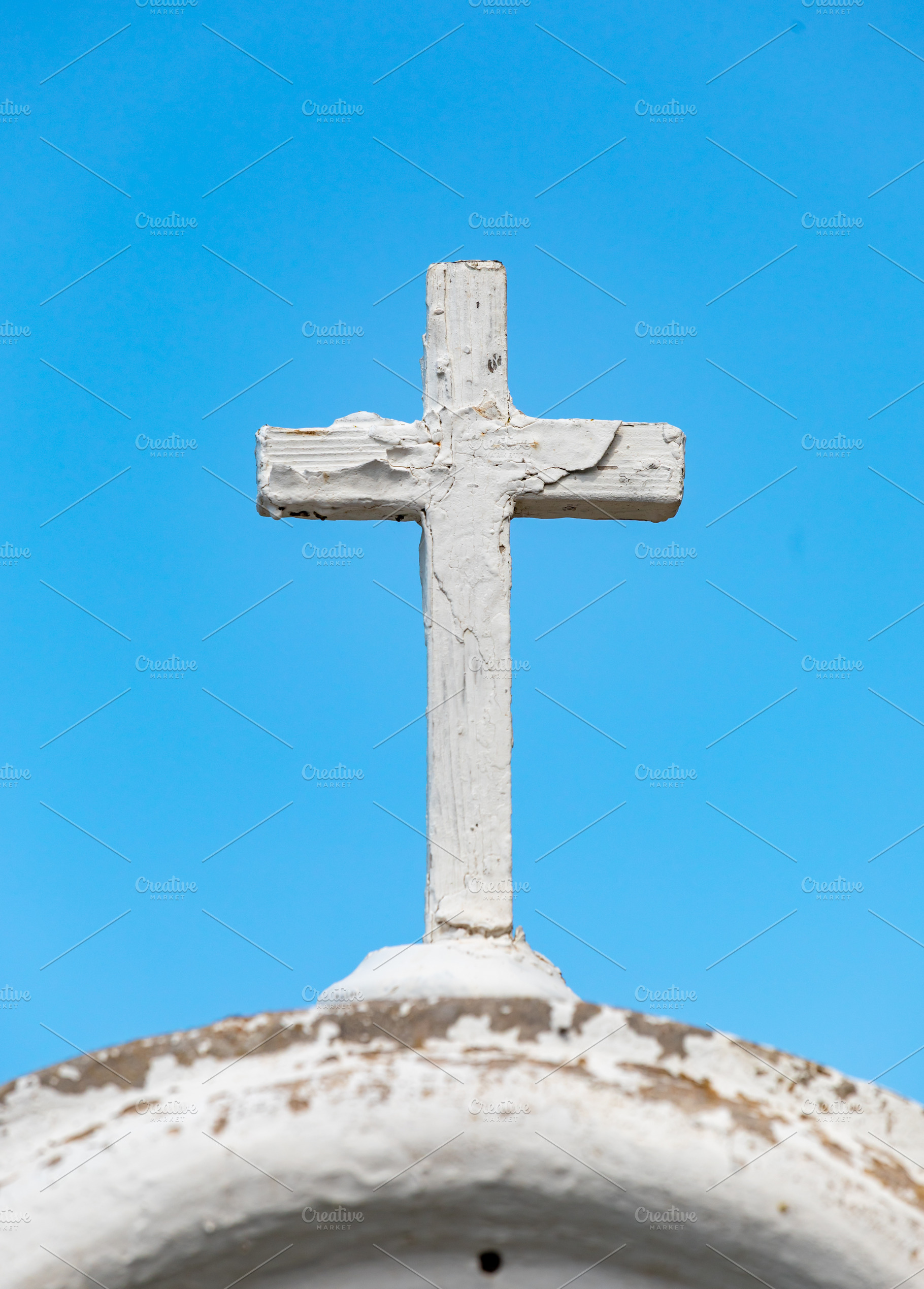 White wooden cross standing on a weathered dome against blue sky, a Photo by Antonio Gravante Market
