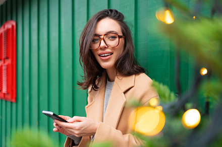 Close up smiling woman using smartphone, standing near Christmas tree, a Person Photo by andreonegin market