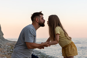 Man and young girl hold hands, sharing a tender moment by the seaside at sunset, a Person Photo by Ales Munt