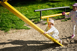 Children playing together on a yellow seesaw in a sunny playground, a Person Photo by AS photostudio