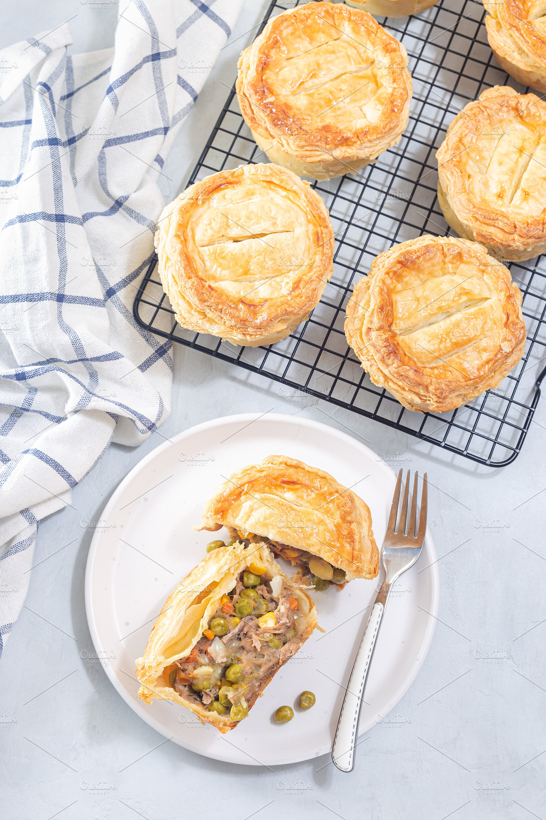 Sliced beef pot pie on plate, pies on cooling rack, vertical, top view, a Food & Drink Photo by iuliia_n