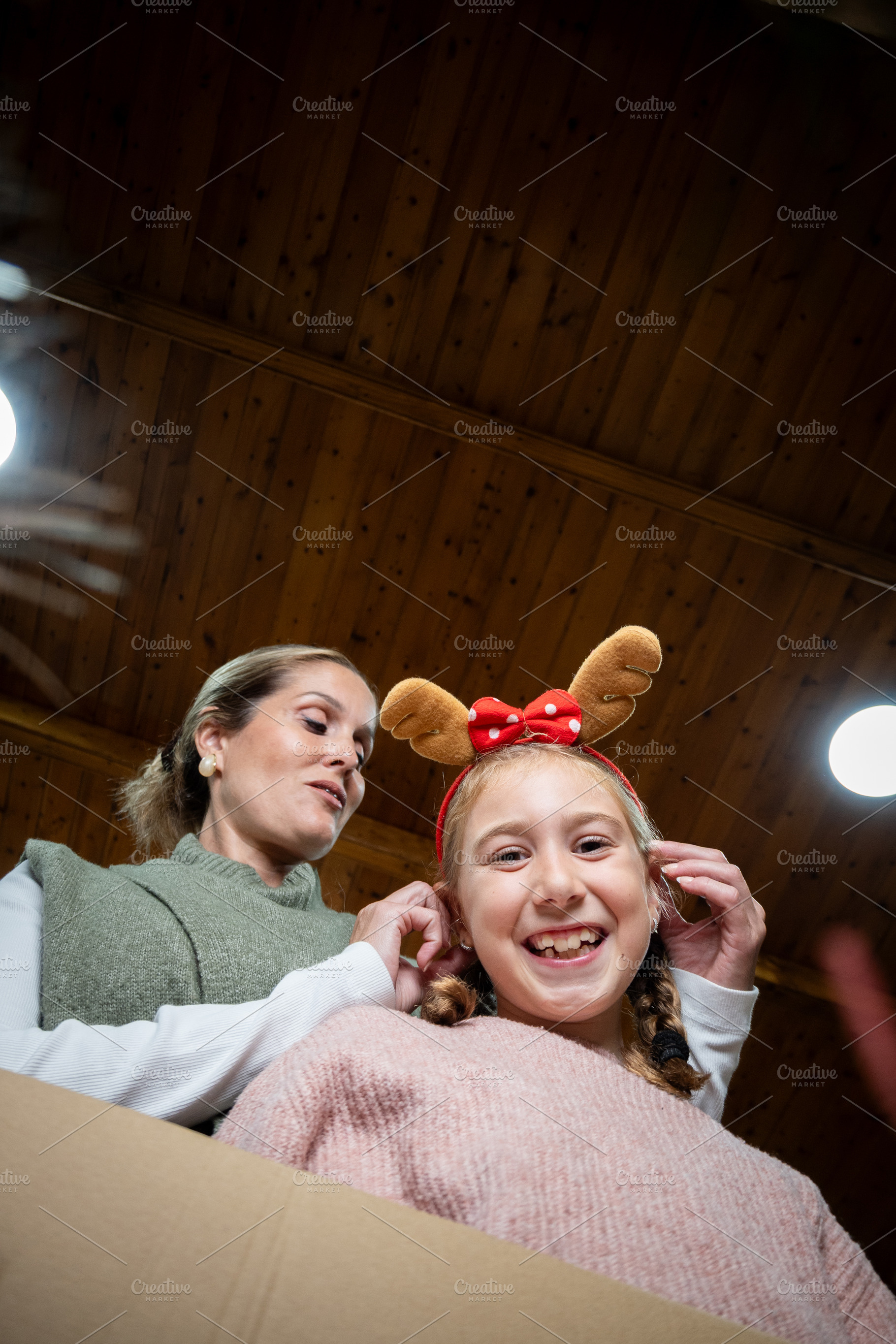 Mother adjusting festive reindeer headband on daughter, a Holiday Photo by etorres69